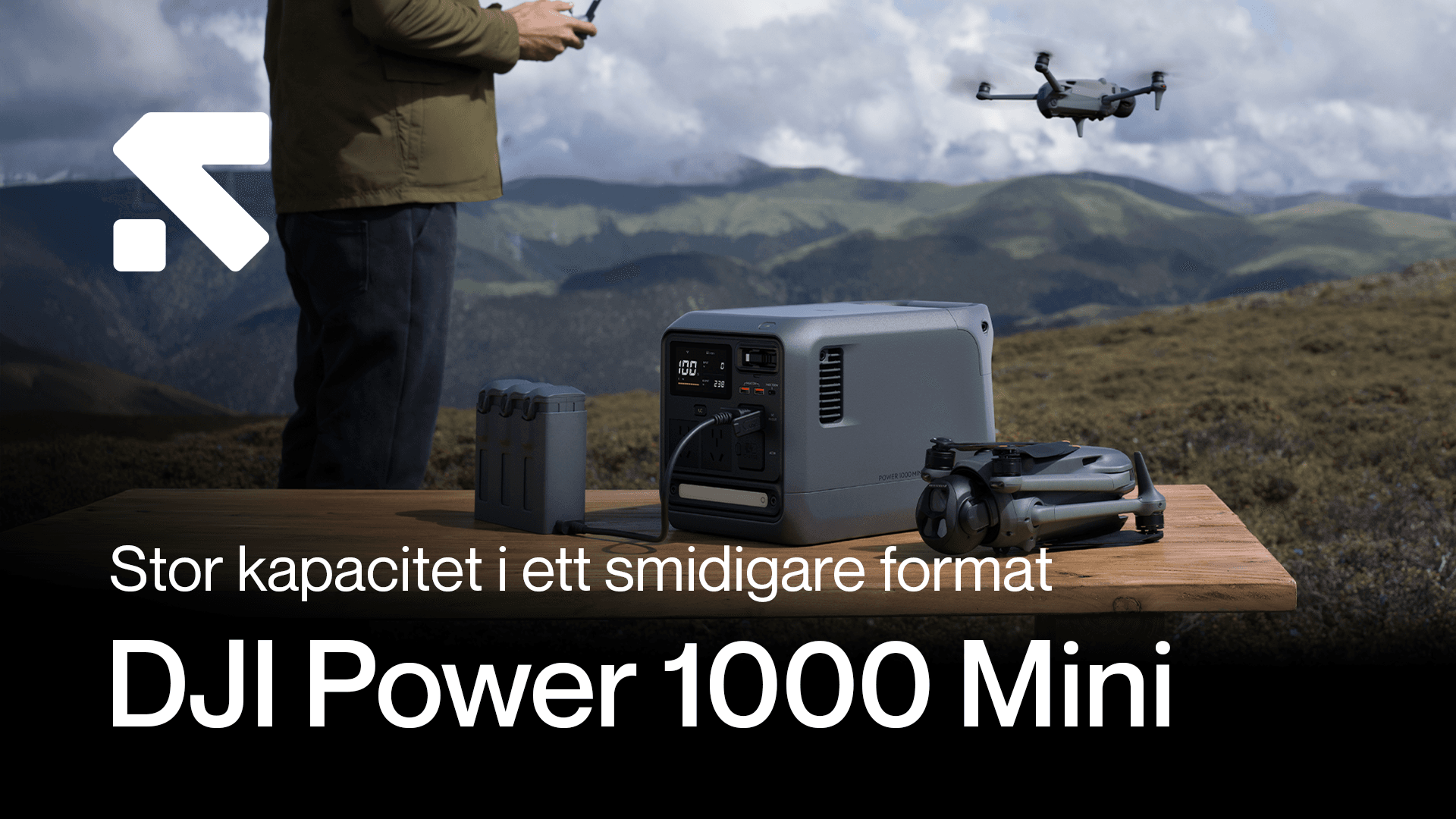 En person står vid ett bord utomhus med en DJI Power 1000 Mini, en drönare och batterier, med berg i bakgrunden.