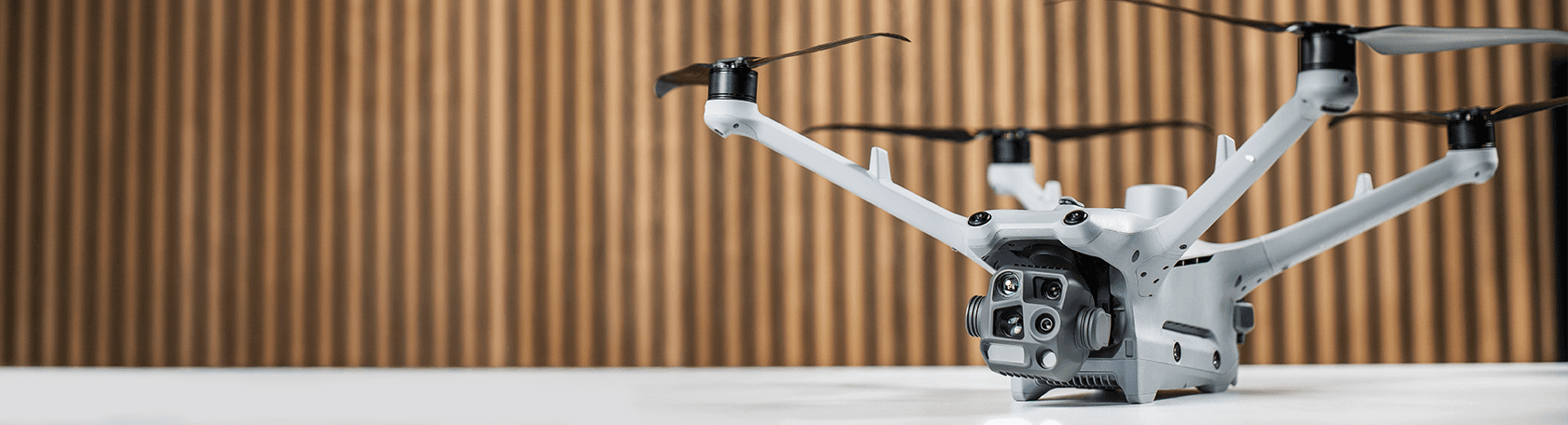 En DJI Matrice 4TD-drönare med flera kameror står på ett bord framför en träpanelvägg.